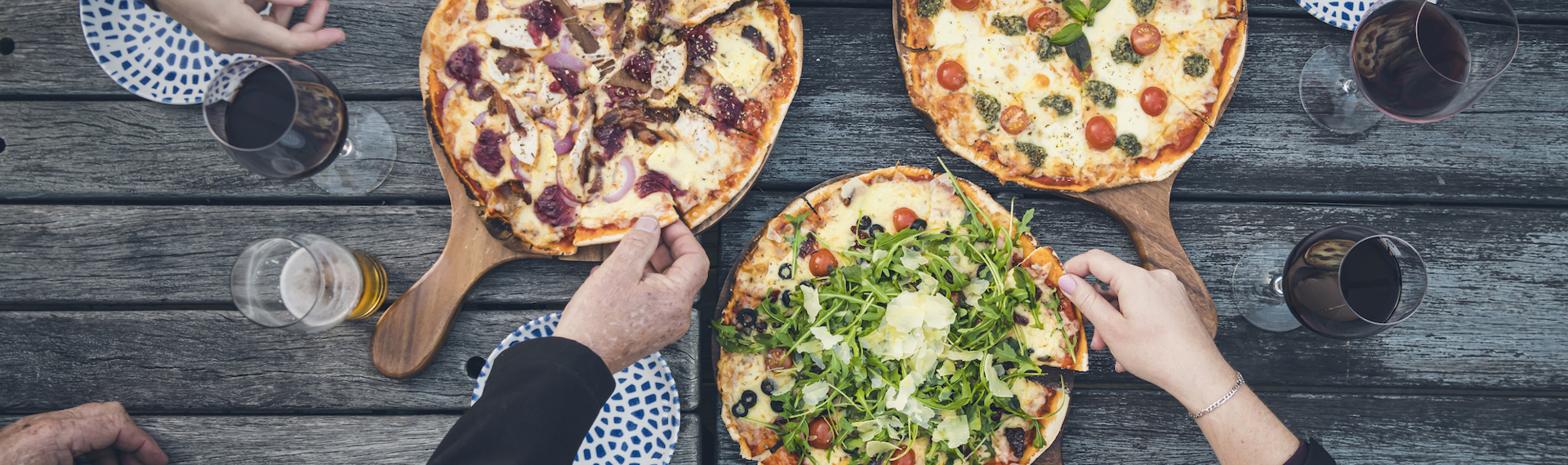 A group of friends share three hot stone baked pizzas and drinks from the Boatshed Cafe and Bar at Punga Cove located in the Marlborough Sounds of New Zealand's South Island