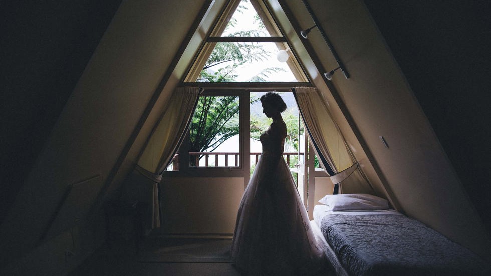 A bride stands at the entrance of a Koru Chalet room at Punga Cove with a scenic lush Punga fern forest outside in the Marlborough Sounds, New Zealand