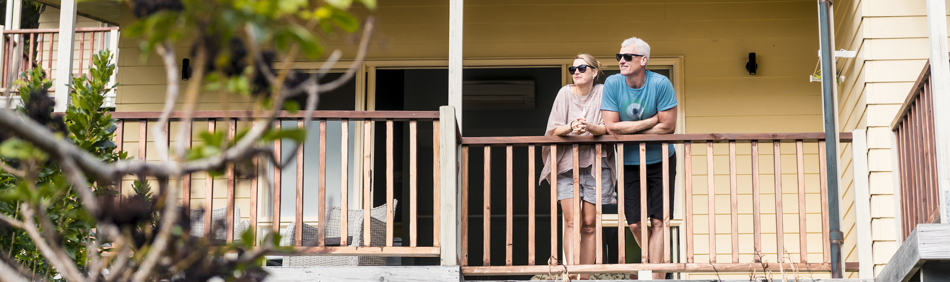 Couple admire scenic Endeavour Inlet views from their Fern Studio balcony at Punga Cove surrounded by Punga ferns in the Marlborough Sounds of New Zealand