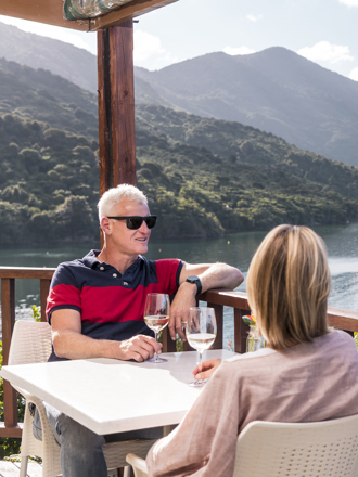 A couple enjoying their glasses of wine from the Punga Fern Restaurant located at Punga Cove with sweeping views of the Endeavour Inlet in New Zealand's top of the South Island Marlborough Sounds.