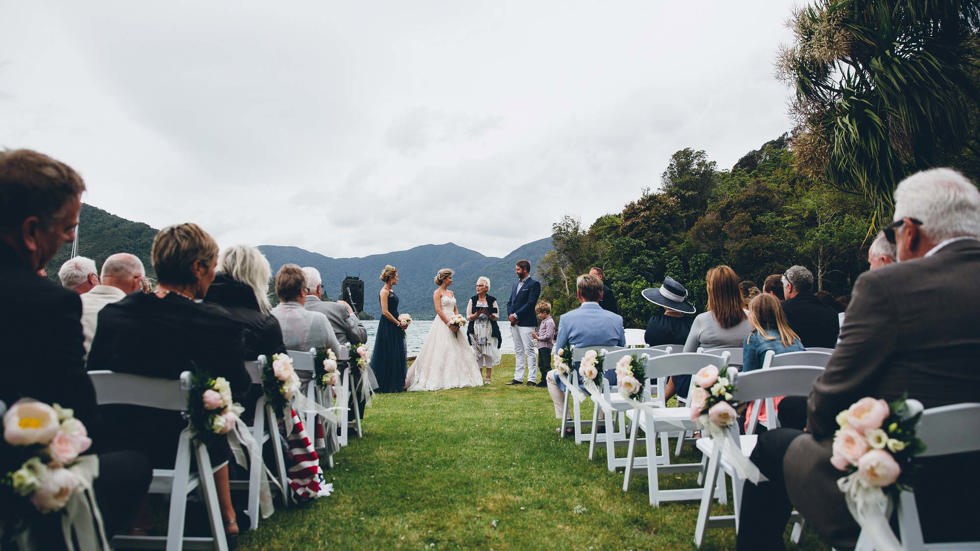 Bride and Groom say their vows at a Punga Cove wedding on the front lawn with seated guests in the Marlborough Sounds of New Zealand