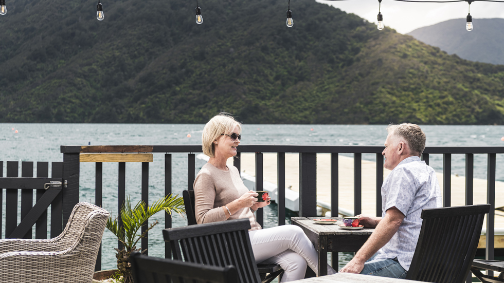 A couple enjoy their coffee at Punga Cove - accompained by views of Endeavour Inlet from the Boatshed Cafe and Bar in New Zealand's South Island Marlborough Sounds