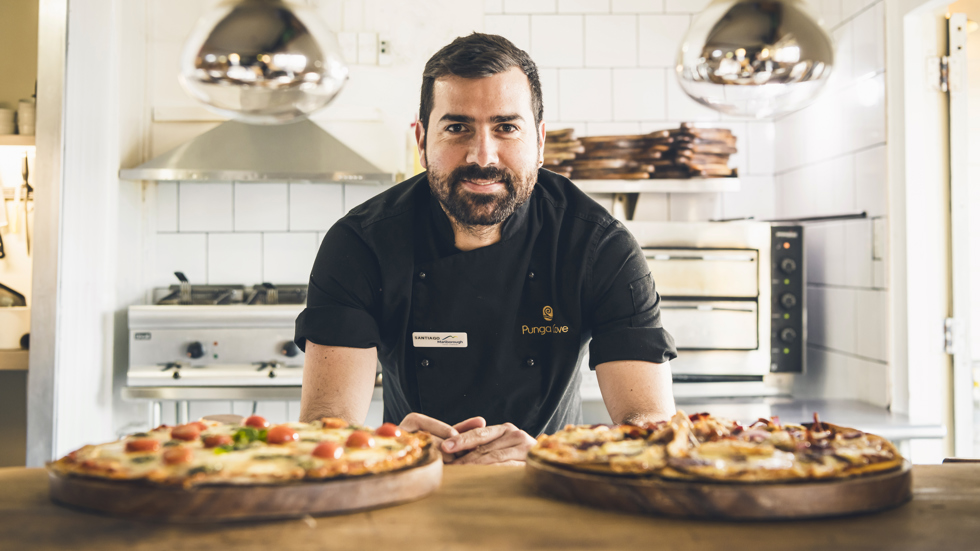 Friendly chef at Punga Cove Boatshed Cafe and Bar serves two fresh hot stone baked pizzas - great to enjoy on the jetty at Punga Cove located in the Marlborough Sounds of New Zealand's South Island