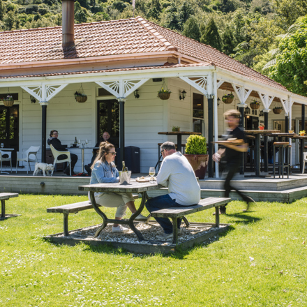 Two people are served by a waiter on the lawn while dining at Furneaux Lodge in the Marlborough Sounds, New Zealand.